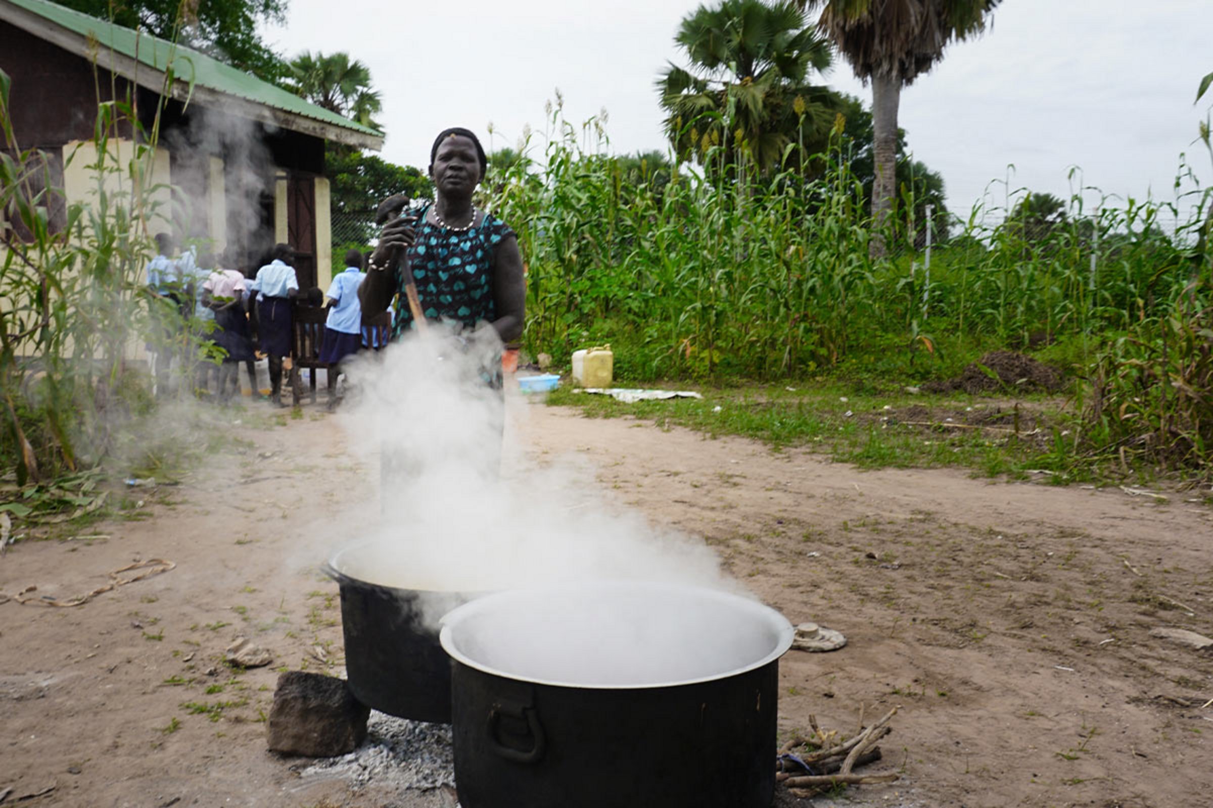 Eine Frau kocht in riesigen Kochtöpfen Mittagessen für Schülerinnen einer südsudanesischen Schule