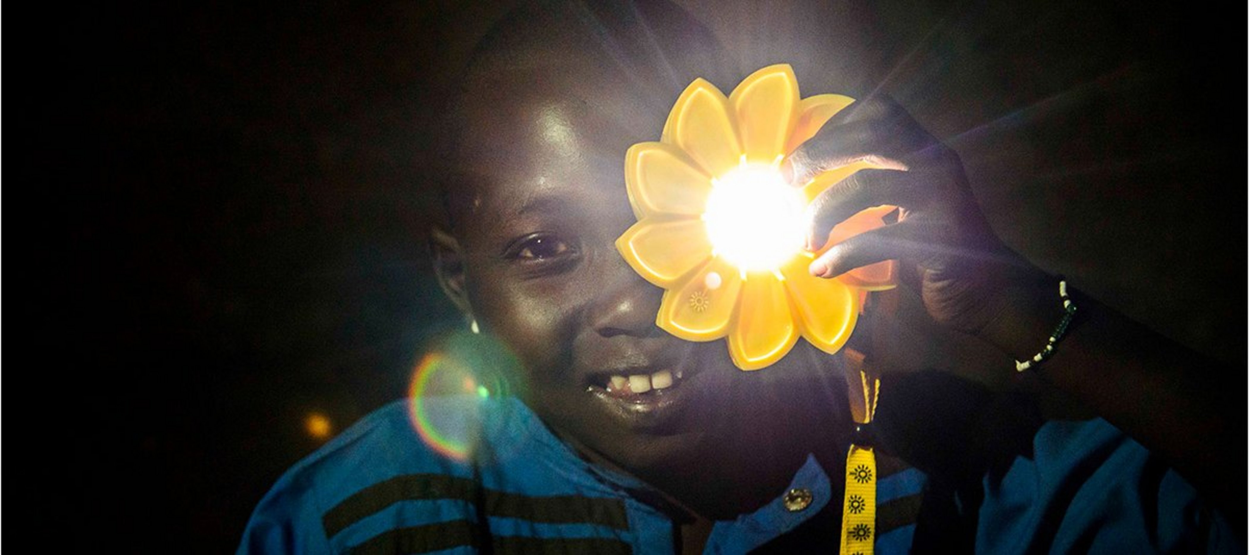 Kind hält leuchtende Little Sun-Solarlampe hoch und lächelt