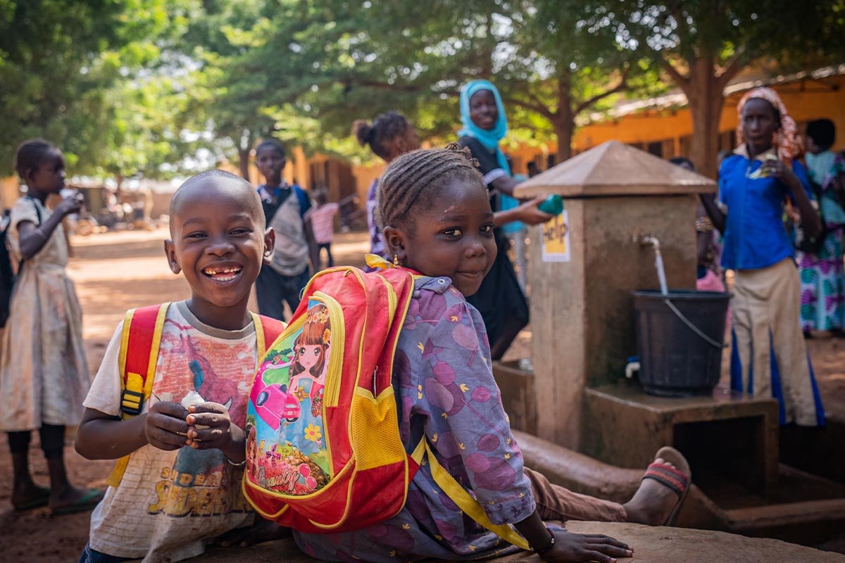 Zwei Schulkinder aus Mali sitzen vor einem Brunnen